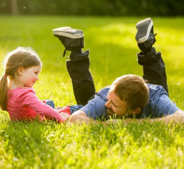A father and daughter lying in th park with luch green grass under the sun