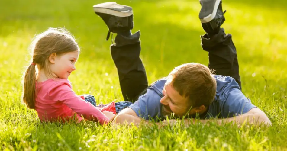 A father and daughter lying in th park with luch green grass under the sun